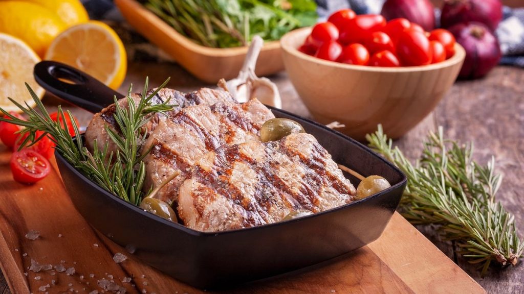 Delicious grilled meat seasoned with rosemary served with fresh vegetables on a wooden board.
